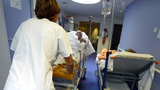 Eine Pflegefachfrau stösst ein Bett mit einem Patienten durch einen Spitalkorridor.