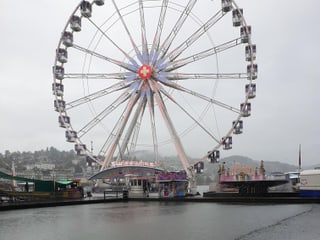 Ein riesen rad steht am Luzerner Messeplatz,  auf der  Seeoberfläche davor erzeugen fallende Regentropfen viele kleine Kreise. 