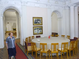 Ein ältere Dame steht neben dem runden Tisch innerhalb des Palasts.
