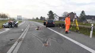 Polizeibeamte arbeiten auf einer Unfallstelle, im Hintergrund zwei stark beschädigte Autos Polizeibeamte arbeiten auf einer Unfallstelle, im Hintergrund zwei stark beschädigte Autos