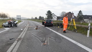 Polizeibeamte arbeiten auf einer Unfallstelle, im Hintergrund zwei stark beschädigte Autos