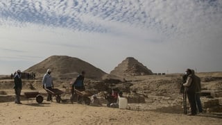 Arbeiter in der Wüste, im Hintergrund eine Stufenpyramide.