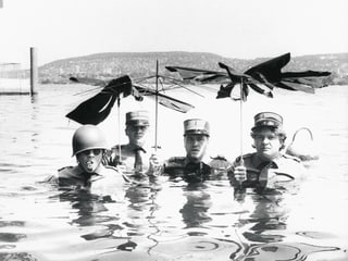 Drei Offiziere stehen im Wasser und halten kaputte Schirme in die Höhe.