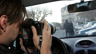 Ein Mann sitzt mit einer Kamera in einem Auto und fotografiert ein Paar.