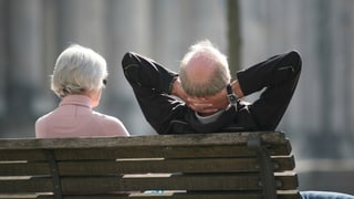 Älterer Mann und ältere Frau sitzen auf einer Bank, fotografiert von hinten.