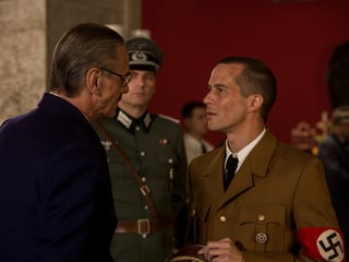Filmstill: Ein Mann im dunklen Anzug unterhält sich mit einem Mann in Nazi-Uniform. Filmstill: Ein Mann im dunklen Anzug unterhält sich mit einem Mann in Nazi-Uniform.