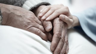 Frauenhand hält die Hände eines älteren Menschen