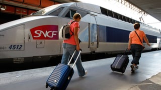 Zwei Reisende mit Rollkoffer gehen einem TGV-Zug entlang.