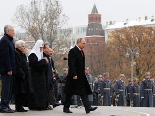 Wladimir Putin läuft zum Rednerpult, umgeben von Gästen und Polizisten.