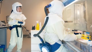 Zwei Wissenchaftler befinden sich in einem Labor und tragen Schutzanzüge mit Sauerstoffzufuhr.