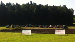 Traktoren der protestierenden Bauern vor der aufgerissenen Wiese. Im Vordergrund zwei Transparente mit der Aufschrift: "Flascher Naturschutz" und "Boden=Leben"