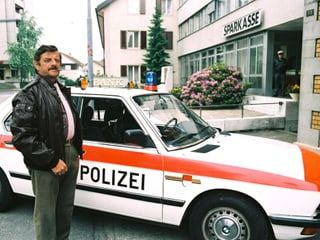 Ein Mann mit Lederjacke steht vor einem Polizeiwagen.