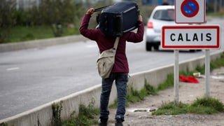Ein Asylsuchender vor einem Calais-Schild.