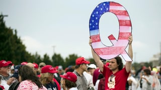 Mann hält an Wahlkampfveranstaltung ein Q aus Karton in die Luft Mann hält an Wahlkampfveranstaltung ein Q aus Karton in die Luft