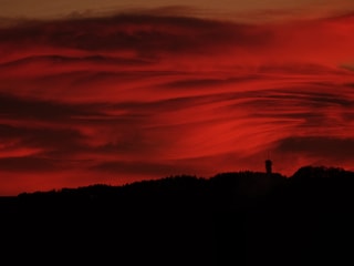 Flammenroter Himmel mit Wolken. Unten Konturen einer Hügelkette mit Turm. 