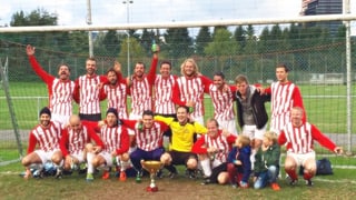 Das Team mit rot-weiss längsgestreiften Shirts posiert mit dem Cup vor dem Goal.