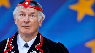 Ein Mann in typischer Schweizer Volkstracht vor der EU-Flagge. 