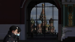 Polizisten mit Gesichtsmasken patrouillieren in Moskau vor dem Auferstehungstor mit der Basilius-Kathedrale im Hintergrund. 