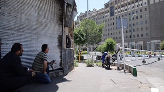 Zwei Männer, einer bewaffnet, beobachten das Parlamentsgebäude aus der Ferne.