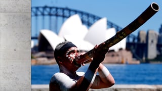 Aborigine mit Didgeridoo, im Hintergrund die Oper von Sidney.