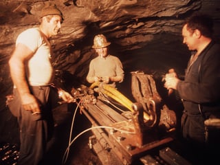 Drei Mineure stehen im rohen Tunnelschacht um eine Maschine