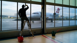 Ein Mann putzt die Scheiben des Rega-Hangars in Kloten, dahinter, draussen, ein Rega-Jet.