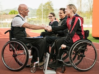 Heinz Frei im Rollstuhl mit den drei Darstellerinnen auf einem Sportplatz.
