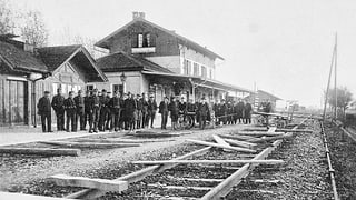 Mehrere Männer stehen an einem Bahnhof