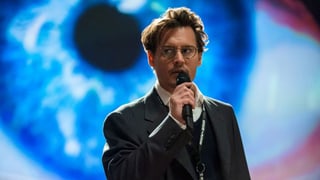 Johnny Depp spricht in ein Mikrophon, im Hintergrund ist ein riesiges blaues Auge projieziert.