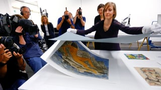 Eine Frau hebt ein Deckblatt von einer Zeichnung ab. Pressefotografen fotografieren. Eine Frau hebt ein Deckblatt von einer Zeichnung ab. Pressefotografen fotografieren.