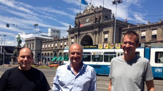 Die drei Männer stehen am Verkehrskonten Bahnhofplatz, im Hintergrund der Zürcher Hauptbahnhof.