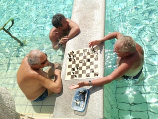 Drei Männer stehen im Wasser und spielen Schach.