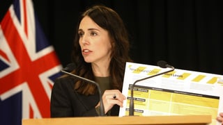 Jacinda Ardern hält ein Covid-19-Plakat hoch.