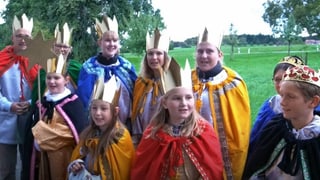 Eine Gruppe von Menschen mit Kindern mit goldiger Krone und Gewand am singen