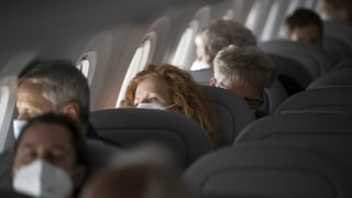Menschen sitzen in einem Flugzeug und tragen eine Gesichtsmaske