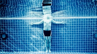 Unterwasserperspektive: Mann steht im Pool, Kopf ist über Wasser.