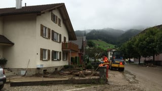 Ein beschädigtes Haus im Hintergrund und Schlamm auf der Strasse davor.