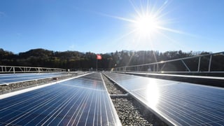 Sonne scheint auf eine Solaranlage in Daillens in der Romandie, Schweizerfahne weht im Hintergrund.