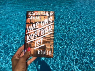 Annette König hält das Buch von Kaouther Adimi: «Was uns kostbar ist» vor blaues Wasser Annette König hält das Buch von Kaouther Adimi: «Was uns kostbar ist» vor blaues Wasser