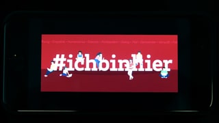 Smartphone mit Titelbild des Facebook-Accounts. Darauf Schriftzug «#ichbinhier».
