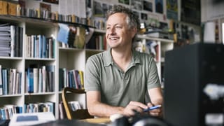 Ein Mann sitzt an seinem Pult in seinem Büro. Hinter ihm viele Bücher, CDs und Fotos. Ein Mann sitzt an seinem Pult in seinem Büro. Hinter ihm viele Bücher, CDs und Fotos.