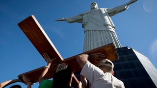 Drei Menschen errichten vor der Jesusstatue auf dem Corcovado in Rio de Janeiro das hölzerne Weltjugendtagskreuz.
