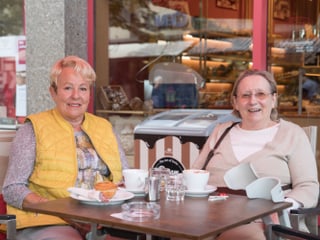 Zwei ältere Frauen sitzen lachend am Tisch einer Bäckerei.