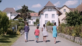 Vier dunkelhäutige Kinder gehen auf einer Dorfstrasse.