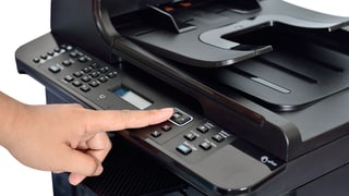 Eine Person drückt auf einen Knopf eines schwarzen Druckers.