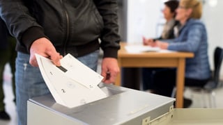 Ein Mann wirft im Wahllokal seine Stimmzettel in die Wahlurne
