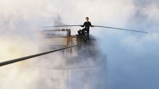 Mann auf einem Seil hoch über den Wolken und auf Höhe der Hochhäuser in New York mit einem langen Balancierstab in der Hand. 