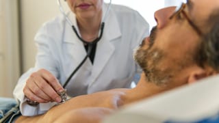 Eine Ärztin hört einen Patienten mit einem Stethoskop ab.