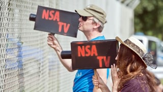 Zwei Menschen mit selbst gebastelten Kameras auf denen "NSA TV" steht.