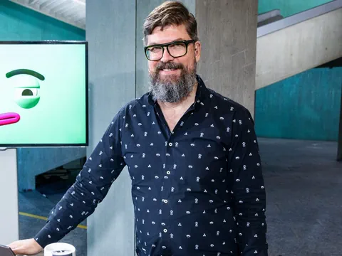 Mann mit Brille und Bart steht vor blauem Hintergrund.